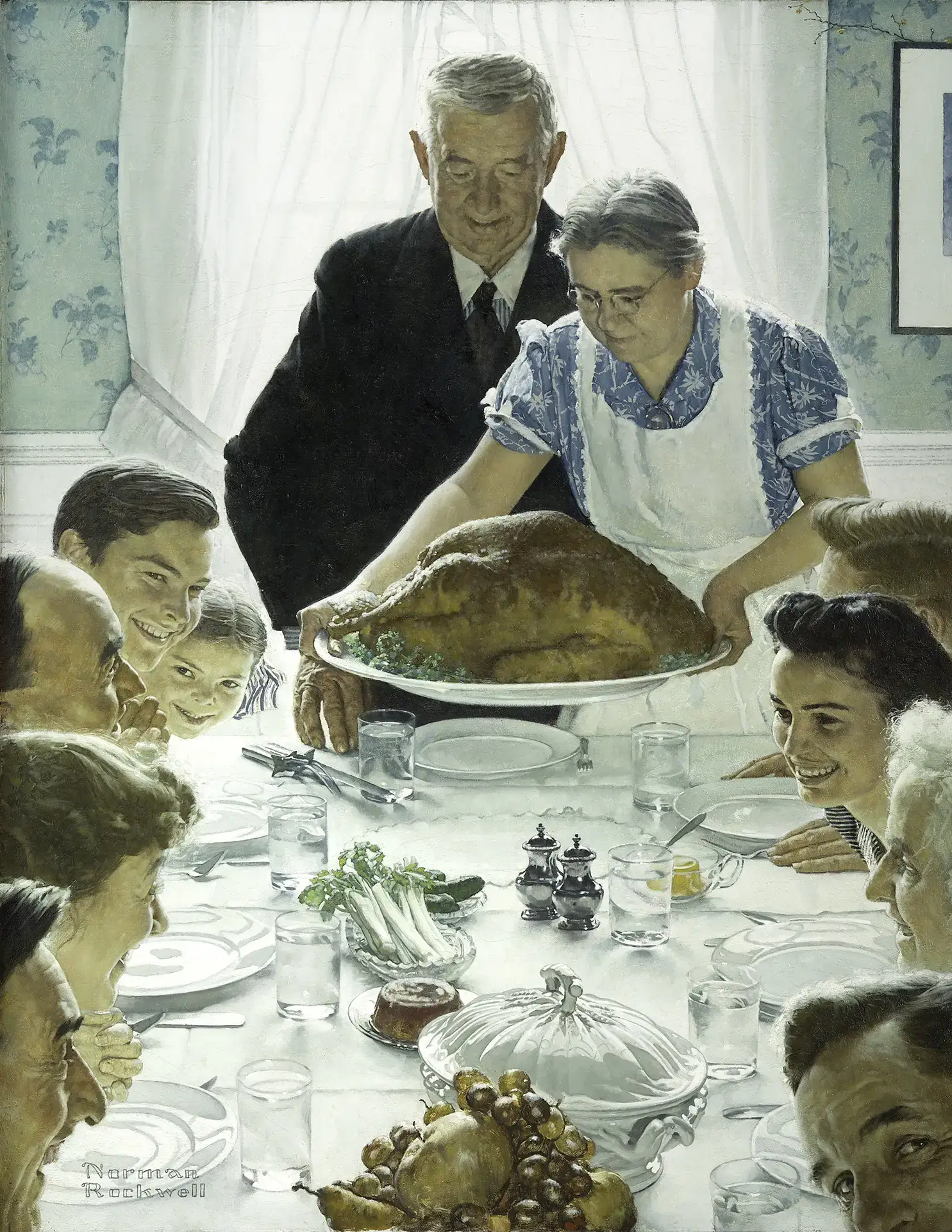 An elderly couple stands at the head of a dining table, with the woman presenting a large roasted turkey. Surrounding the table, family members of various ages anticipate the meal, smiling and engaging with each other.